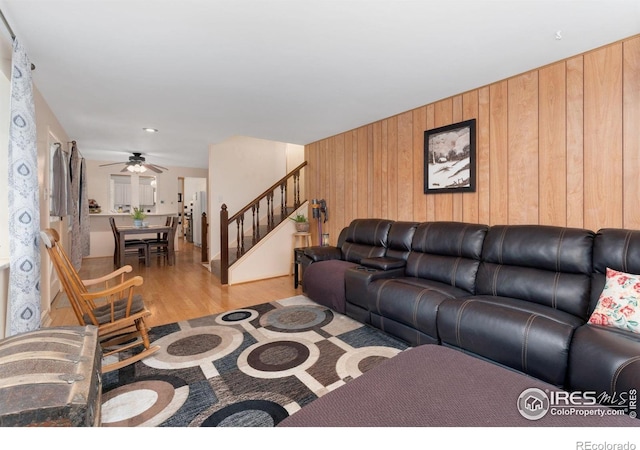 living area with stairway, ceiling fan, light wood finished floors, and wood walls