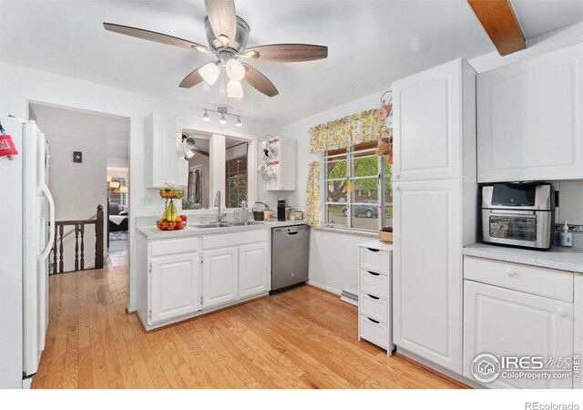kitchen with stainless steel dishwasher, a sink, freestanding refrigerator, light countertops, and white cabinetry