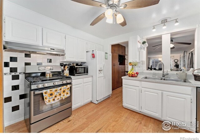 kitchen featuring stainless steel appliances, under cabinet range hood, ceiling fan, a sink, and light wood-type flooring