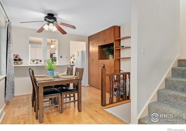 dining space with a ceiling fan, light wood-type flooring, and stairs