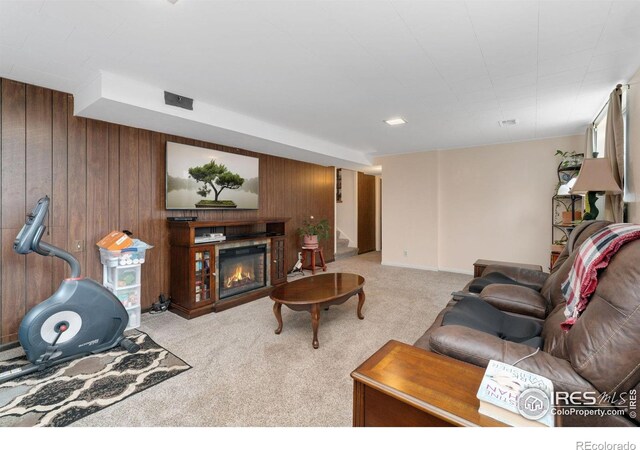 carpeted living room with wood walls, stairway, and a glass covered fireplace