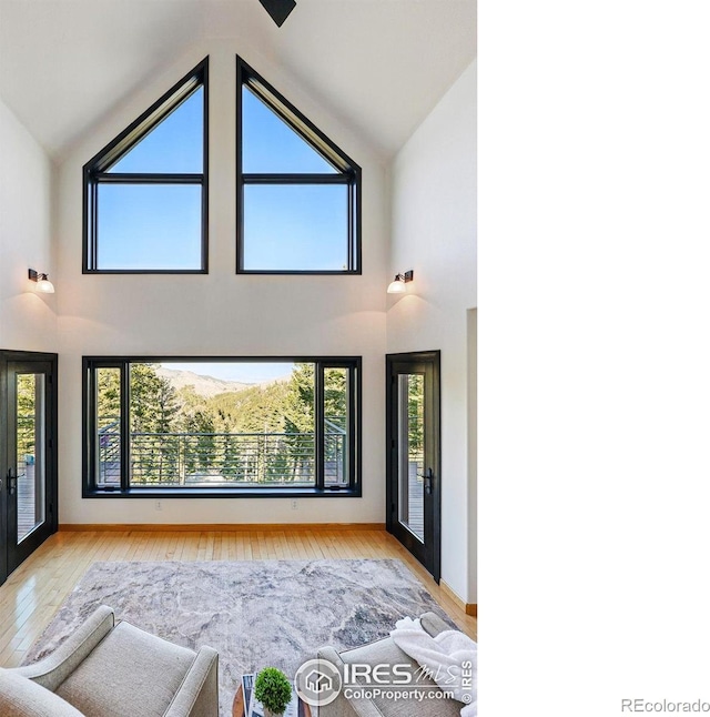 unfurnished living room with high vaulted ceiling, wood finished floors, plenty of natural light, and baseboards