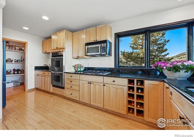 kitchen with light brown cabinets, stainless steel appliances, light wood-style floors, dark stone countertops, and recessed lighting