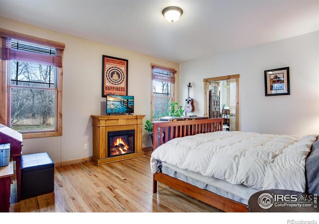 bedroom featuring wood finished floors, baseboards, and a glass covered fireplace