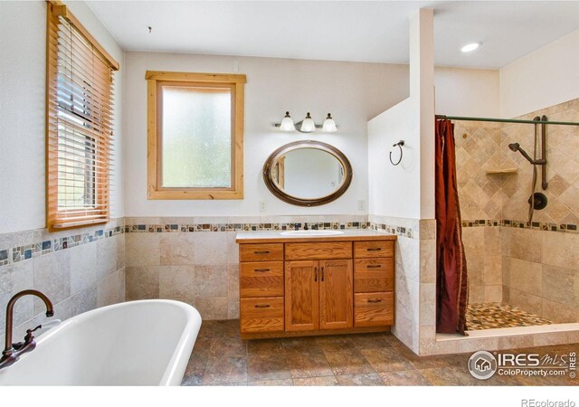 bathroom featuring tile walls, tiled shower, a freestanding bath, vanity, and a wainscoted wall