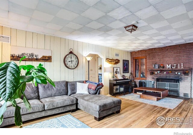 living room with wood finished floors, arched walkways, a drop ceiling, wooden walls, and a large fireplace