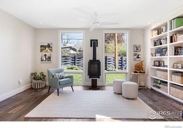 living area with wood finished floors, ceiling fan, baseboards, recessed lighting, and a wood stove