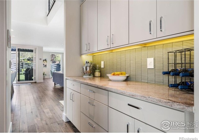 kitchen with wood finished floors, tasteful backsplash, baseboards, and light stone counters