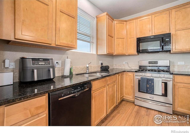 kitchen with black appliances, a sink, light wood-style floors, dark stone countertops, and light brown cabinets