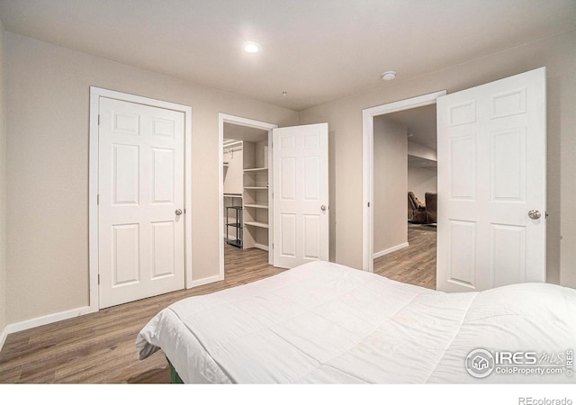 bedroom featuring wood finished floors, baseboards, recessed lighting, and a walk in closet