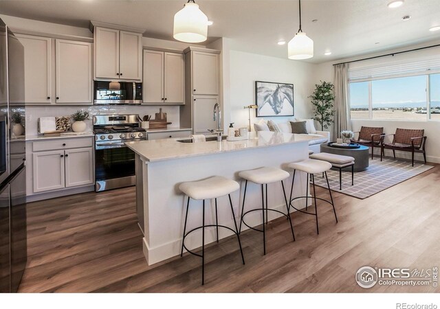 kitchen with appliances with stainless steel finishes, a sink, dark wood-style flooring, a kitchen bar, and recessed lighting