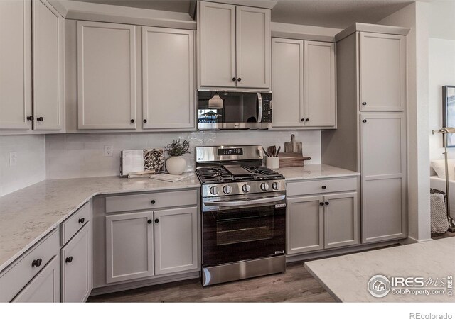 kitchen featuring stainless steel appliances, wood finished floors, and light stone counters