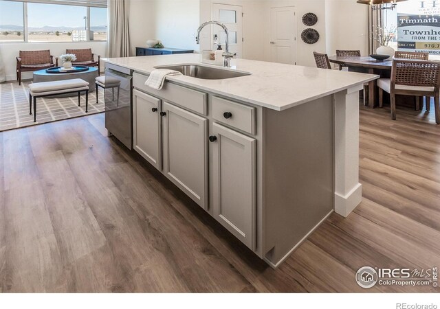 kitchen featuring a sink, dishwasher, dark wood finished floors, an island with sink, and gray cabinetry
