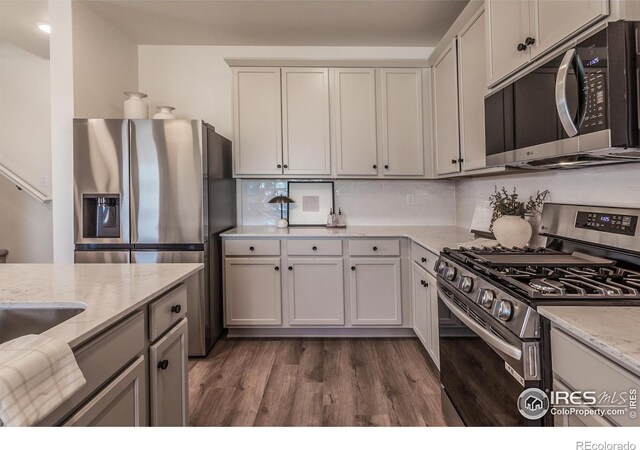 kitchen with appliances with stainless steel finishes, dark wood-style flooring, light stone counters, and tasteful backsplash