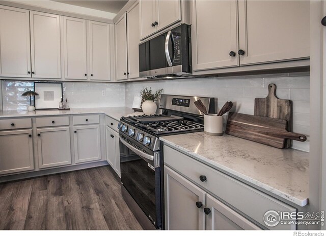 kitchen with stainless steel appliances, backsplash, dark wood-style flooring, and light stone countertops
