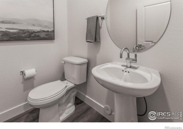 half bath featuring toilet, wood finished floors, baseboards, and a sink