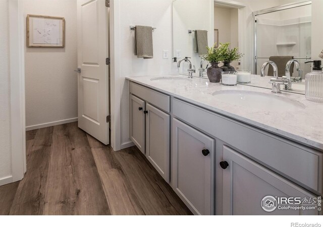 bathroom featuring wood finished floors, double vanity, baseboards, and a shower with door