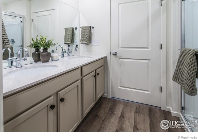 full bathroom with wood finished floors, double vanity, and a shower with shower door