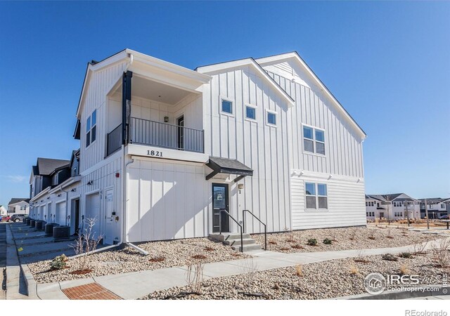 modern farmhouse featuring board and batten siding, a balcony, central AC unit, and an attached garage