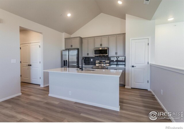 kitchen with stainless steel appliances, gray cabinetry, a sink, an island with sink, and tasteful backsplash