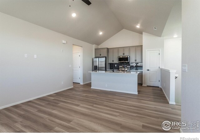 kitchen with appliances with stainless steel finishes, gray cabinets, high vaulted ceiling, ceiling fan, and a center island with sink