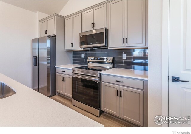 kitchen featuring appliances with stainless steel finishes, gray cabinetry, backsplash, and light countertops