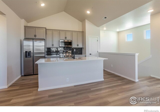 kitchen with stainless steel appliances, gray cabinets, a sink, decorative backsplash, and an island with sink