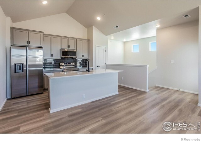 kitchen with appliances with stainless steel finishes, gray cabinets, decorative backsplash, light countertops, and light wood-type flooring