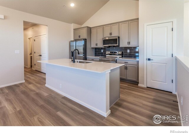 kitchen featuring stainless steel appliances, gray cabinetry, a sink, dark wood-type flooring, and high vaulted ceiling