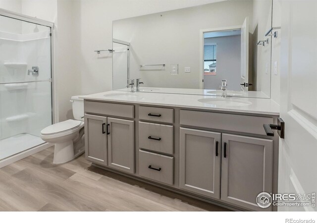 full bath featuring a shower stall, double vanity, wood finished floors, and toilet
