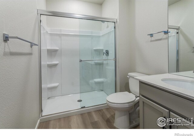bathroom with wood finished floors, a shower stall, vanity, toilet, and a textured wall