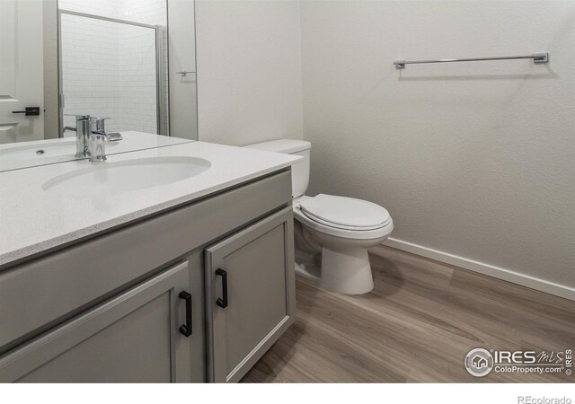 full bath featuring vanity, a shower with door, wood finished floors, toilet, and baseboards