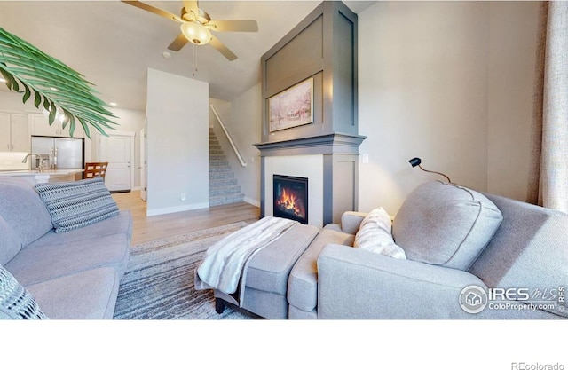 4157 Trapper Lake Dr, Loveland, CO 80538 - living area featuring light wood-style flooring, a ceiling fan, baseboards, a glass covered fireplace, and stairway