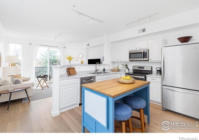 kitchen with stainless steel appliances, track lighting, a sink, white cabinetry, and butcher block counters