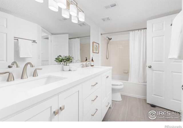 full bath featuring double vanity, shower / tub combo with curtain, a textured ceiling, and toilet