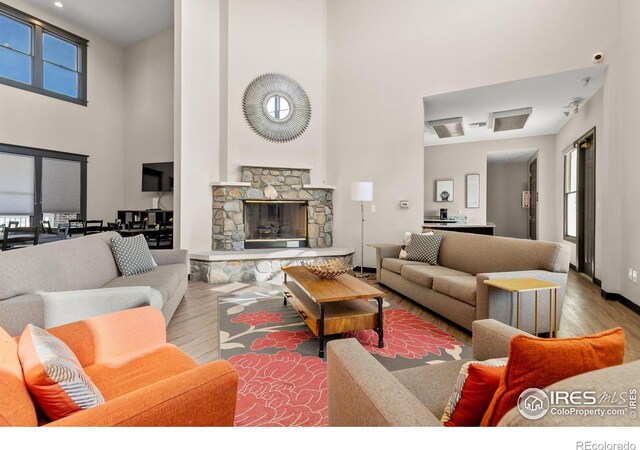 living room featuring wood finished floors, a towering ceiling, healthy amount of natural light, and a stone fireplace