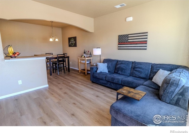 living area featuring a chandelier, arched walkways, light wood-type flooring, and baseboards