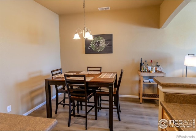 dining room with wood finished floors, a chandelier, baseboards, and a bar
