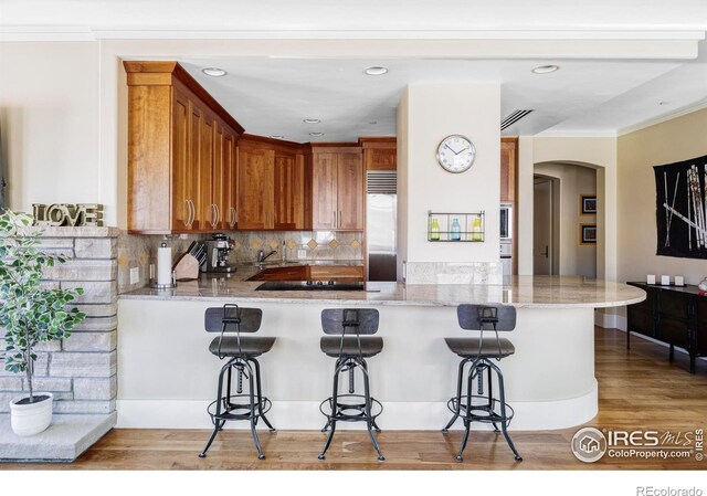 kitchen featuring arched walkways, stainless steel built in fridge, brown cabinetry, a kitchen breakfast bar, and decorative backsplash