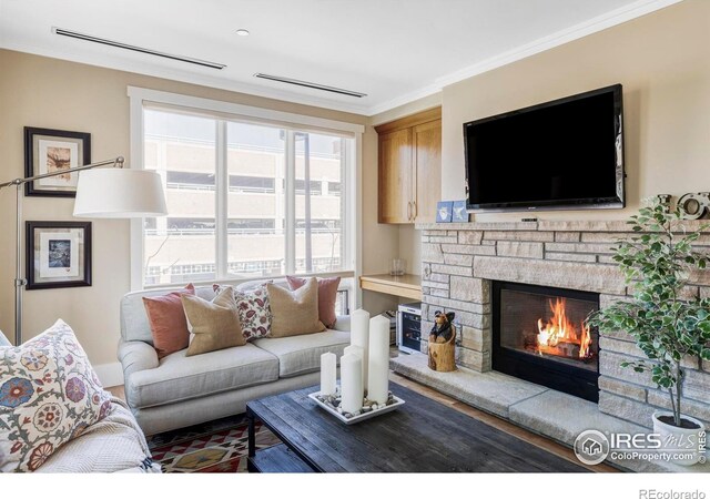 living area featuring crown molding, a stone fireplace, and wood finished floors