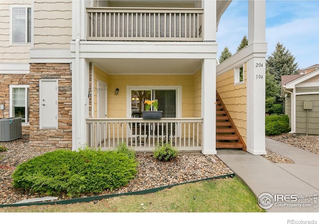 entrance to property with a balcony, stone siding, and central air condition unit