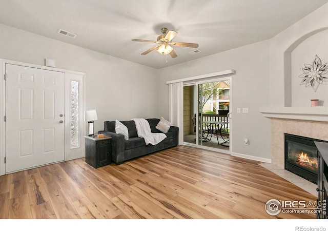 living area with light wood-style flooring, ceiling fan, a tiled fireplace, and baseboards