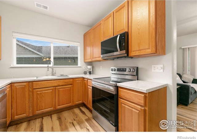 kitchen with stainless steel appliances, a sink, light wood-style floors, and plenty of natural light