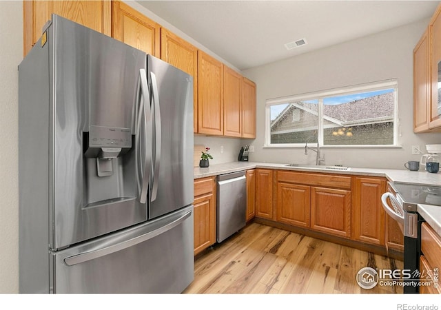 kitchen with stainless steel appliances, a sink, light wood-type flooring, and light countertops