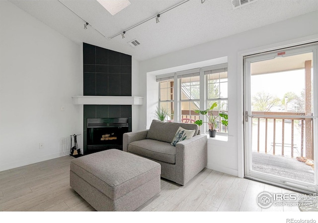 3090 W 107th Pl Unit C, Westminster, CO 80031 - living area featuring rail lighting, light wood finished floors, a tile fireplace, a skylight, and a textured ceiling