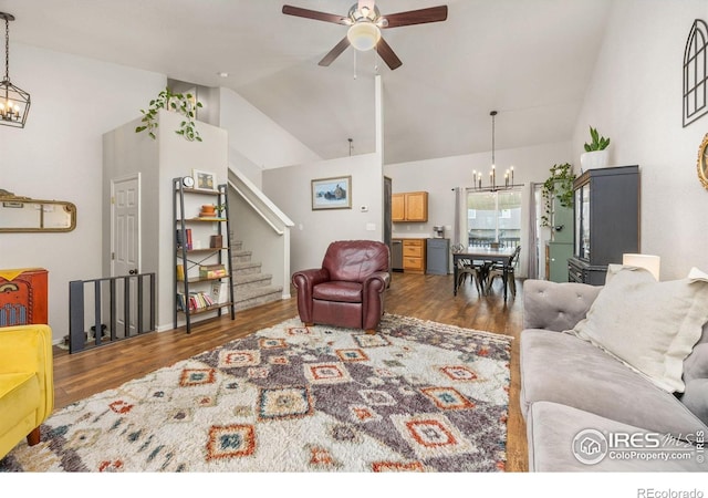 living room with a chandelier, a ceiling fan, wood finished floors, stairs, and high vaulted ceiling