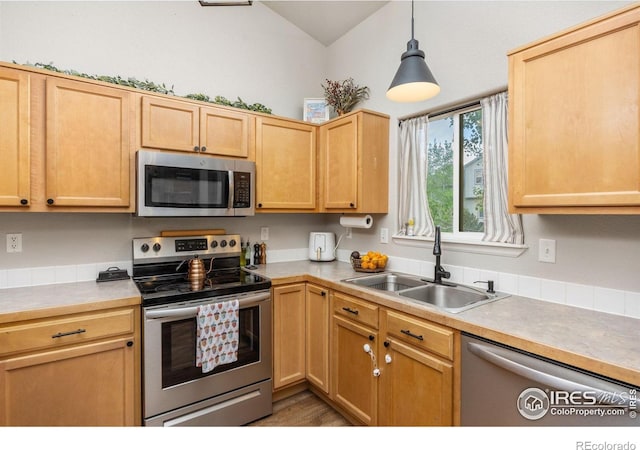 kitchen featuring stainless steel appliances, a sink, light countertops, lofted ceiling, and light brown cabinetry