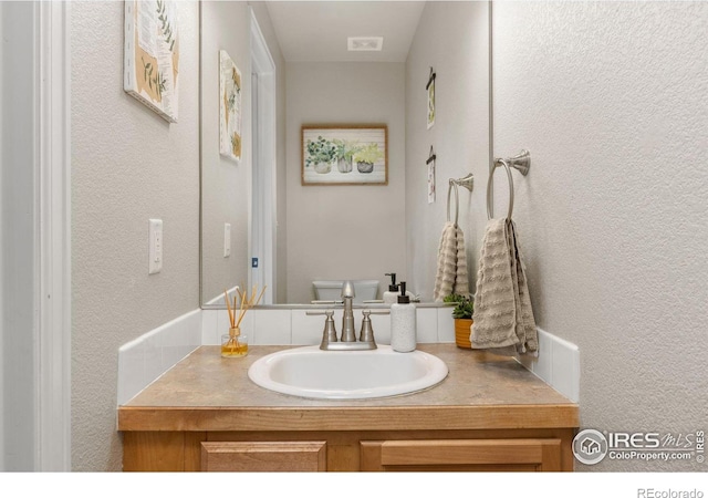 bathroom featuring a textured wall, vanity, and toilet