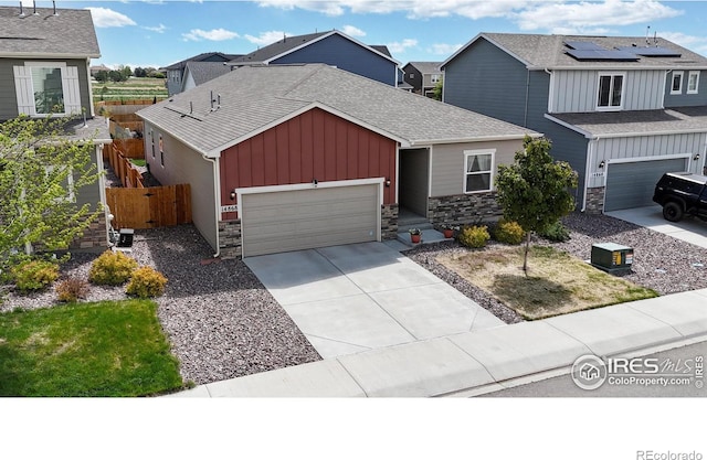 view of front of home featuring board and batten siding, stone siding, concrete driveway, roof with shingles, and fence