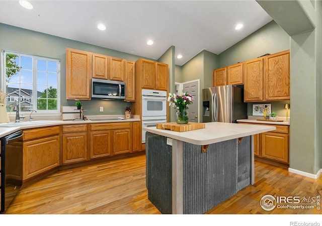 kitchen with appliances with stainless steel finishes, a sink, light wood-type flooring, light countertops, and a kitchen island